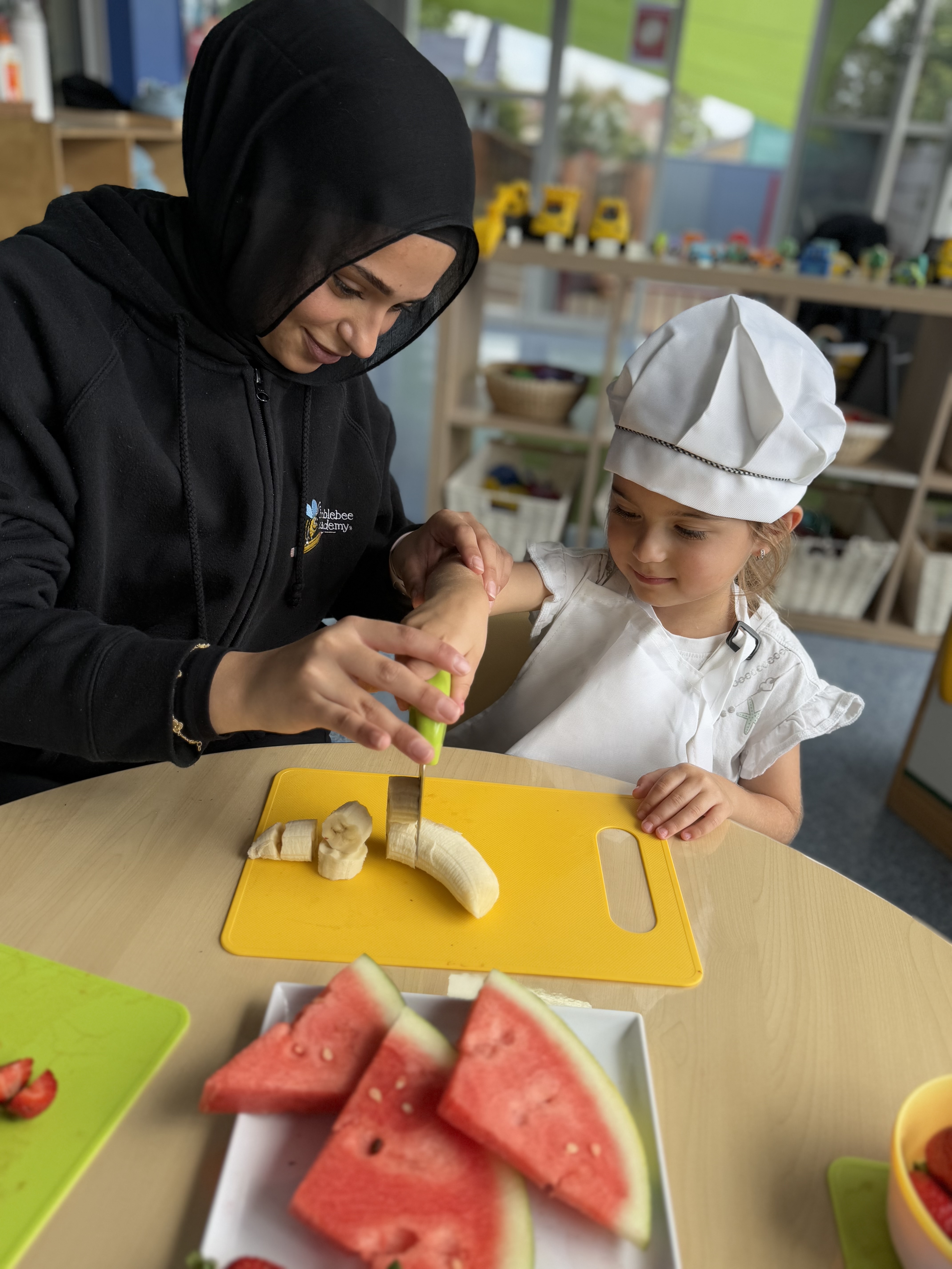Child and educator working together to prepare a banana for snack.